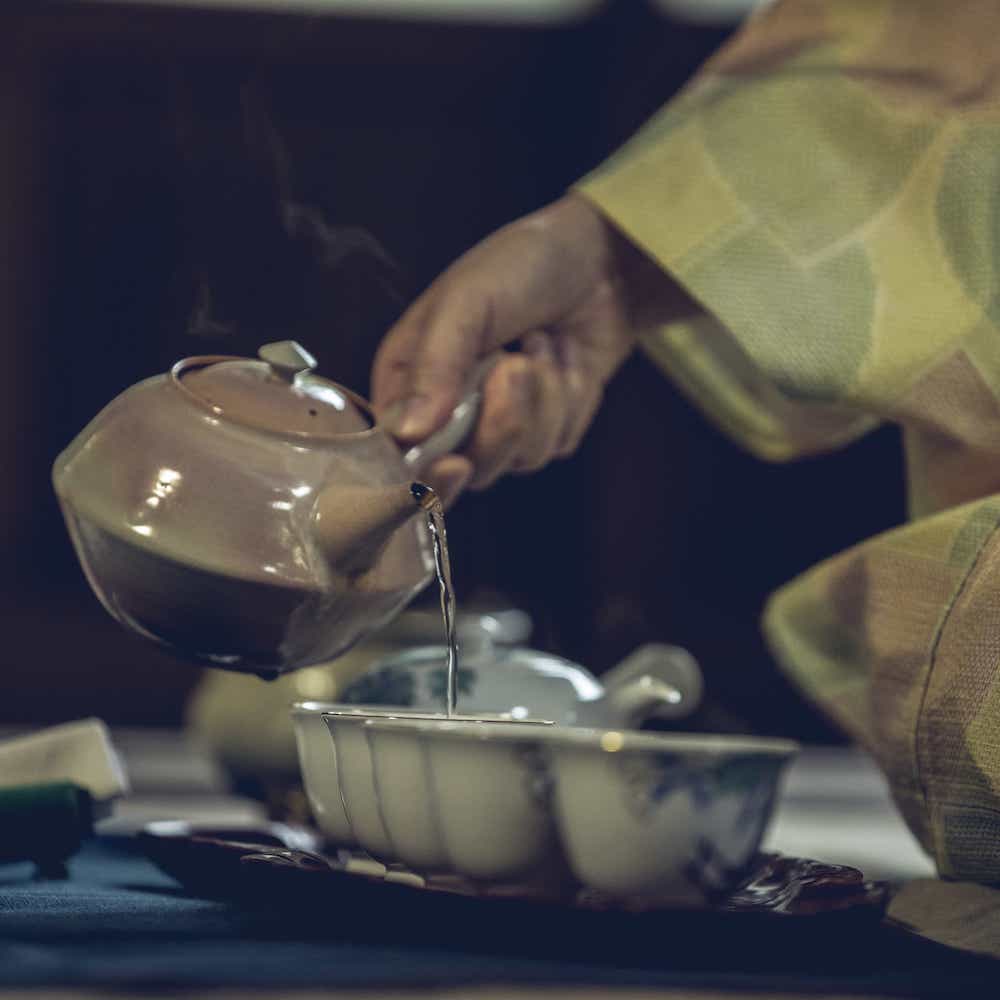 Green tea being poured from a ceramic kyusu into small teacups